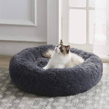 Fluffy white cat lounging comfortably in a soft dark gray round anxiety relieving pet bed near a bright window
